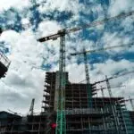 Urban construction site with numerous cranes framing rising skyscrapers against a blue sky.